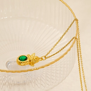 Close-up of a gold Cupid angel pendant necklace featuring a polished round green gemstone