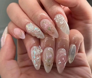 Macro detail of almond press-on nails with 3D floral, butterfly, and pearl accents