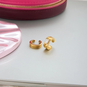 Dettaglio del ear cuff dorato con zircone a goccia e gemma marquise su sfondo grigio