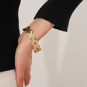 Close-up of golden hammered metal cuff bracelet with circular hollow design on model wrist