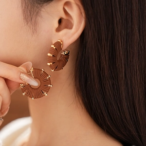 Detailed close-up of brown woven leather texture on C-shaped earrings with gold metal beads