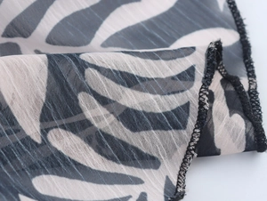 Close-up of black and white leaf print chiffon fabric with delicate hem stitching