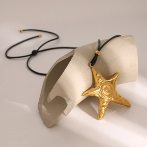 Vintage 18k gold starfish pendant on black cord necklace displayed on ceramic