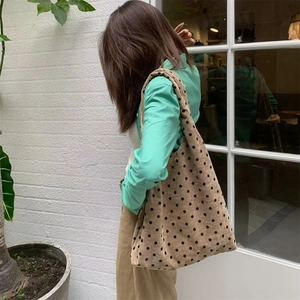 Polka dot corduroy tote bag worn by model against a white brick wall background