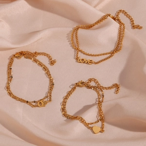 Detail of gold double-layer chains with heart, hand of Fatima and Love charms on pink silk