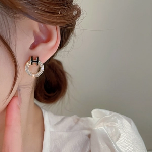 Close-up of zircon hoop earrings with a black enamel letter H and silver needle studs