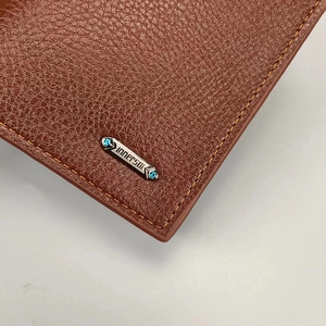 Primer plano de cartera de cuero marrón con grano de lichi y logo de metal