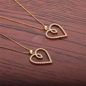 Detailed close-up of two gold heart necklaces with zircon pavé on a dark wooden surface
