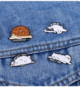 Close-up of cute hedgehog, seal, sheep and cat enamel pins on blue denim fabric