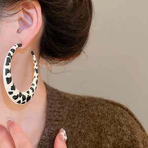 Close-up of model wearing large C-shaped earrings with black and white cow print texture