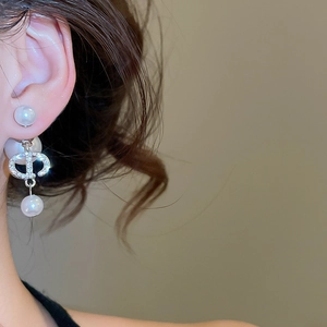 Macro detail of silver pearl drop earring featuring rhinestone encrusted logo design