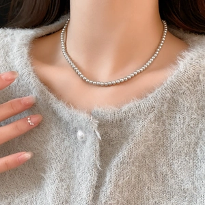 Close-up of small 3-4mm grey pearl necklace worn on collarbone with soft texture sweater