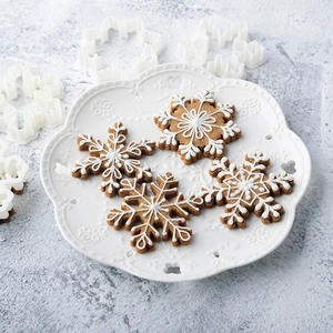 Set of snowflake cookie cutters with iced gingerbread cookies on a white plate