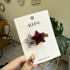 Star-shaped hair clip with wine red and plaid bow design on a branded card