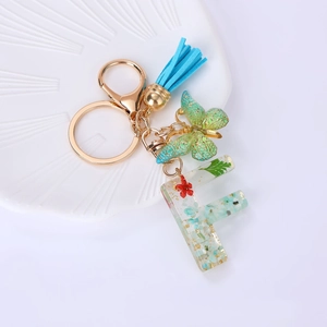 Macro view of letter F resin keychain with real dried flowers, gold butterfly and blue tassel