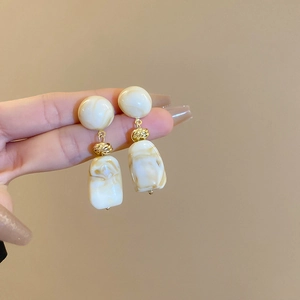 Detail of cream marble resin drop earrings with elegant golden metal knot link