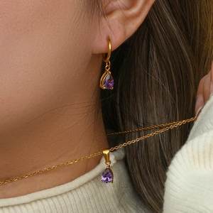 Detalle de pendientes chapados en oro y colgante de circón morado en una modelo