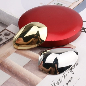 Macro detail of polished gold and silver metal egg-shaped hair clips on a red pedestal