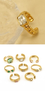 Detail of gold-plated rings with colorful zircon inlays on textured glass background