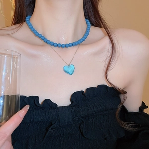 Close-up of double layer necklace featuring blue beads and a clear heart-shaped pendant