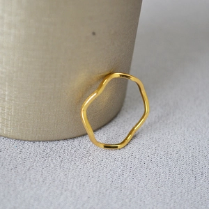Dettaglio macro di un anello minimalista ondulato in ottone placcato oro lucido