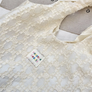 Detail of 3D floral lace tote bag featuring colorful embroidered brand tag on cream fabric