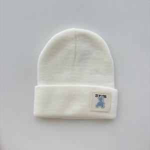 Close-up of white ribbed knit beanie featuring a stitched blue bear embroidery patch