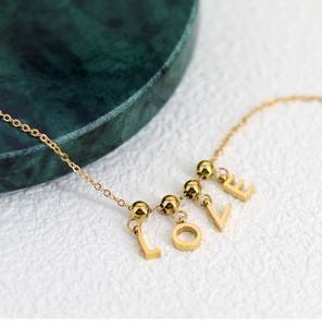 Detail of a gold-finish DIY necklace featuring LOVE letter pendants and metallic beads