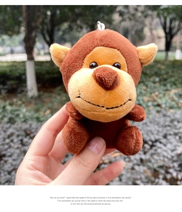 Macro shot of a cute brown plush monkey keychain held against a blurred park background