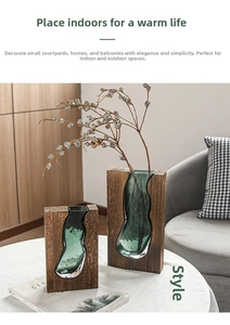 Close-up of modern wood frame and dark green glass vase set on a white table