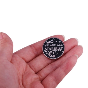 Black enamel pin badge with silver We Are All Stardust text and celestial patterns