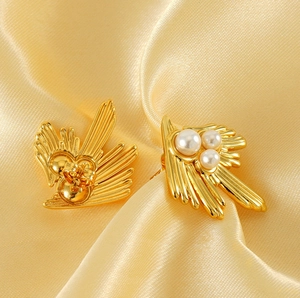 Macro shot of 18K gold-plated swallow wing earrings with white pearls on champagne silk
