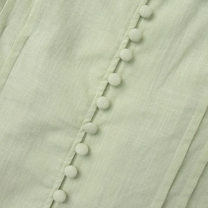 Macro detail of mint green cotton set featuring fabric buttons and pleated textures