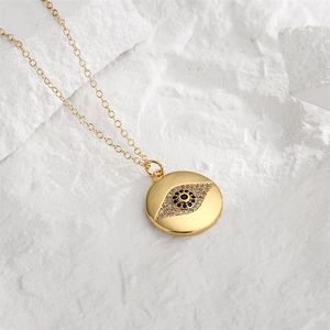 Close-up of gold evil eye pendant necklace with blue zircons on white marble