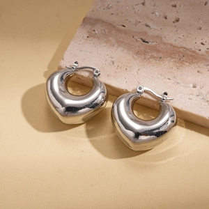 Macro view of silver 3D heart hoop earrings with polished mirror finish on stone surface