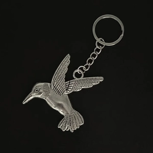 Silver hummingbird keychain with detailed feather carvings and a metal ring on black background