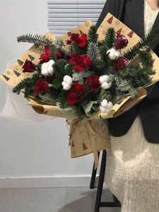 Christmas bouquet with red roses and pine branches wrapped in snowflake gift paper