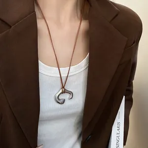 Minimalist silver irregular C-pendant necklace with brown cord on a model in brown blazer