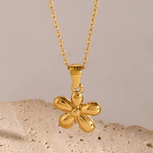 Macro shot of gold stainless steel five-petal flower pendant on a beige stone surface