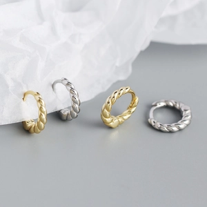 Macro view of gold and silver twisted rope hoop earrings on artistic pleated paper