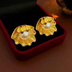 Close-up of golden shell earrings with white pearls in a red velvet jewelry box