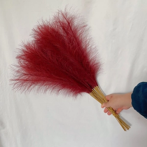 Handheld bundle of deep red artificial pampas grass with fluffy feathers and tan stems