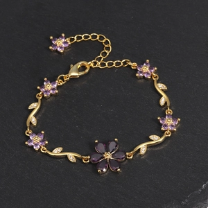 Detail eines goldene Blumenarmbands mit violetten Zirkonia-Blüten auf schwarzer Oberfläche