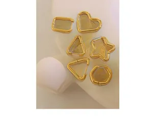 Macro detail of six geometric gold earrings including heart and star shapes on warm props