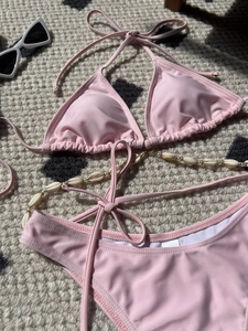 Detail of pink bikini with shell chain and gold beads on a textured background
