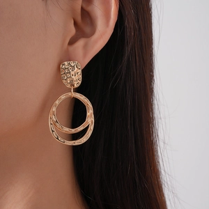 Détail de boucles d'oreilles géométriques dorées avec texture martelée et anneaux
