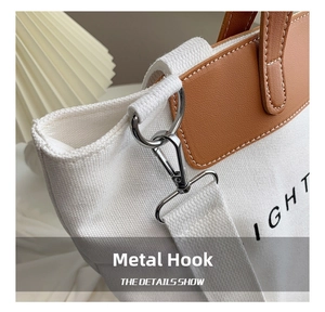 Detail of silver metal hook and brown leather trim on canvas tote bag with letters
