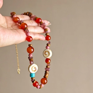 Detail of handcrafted beaded necklace with agate, wood, and turquoise beads held in hand