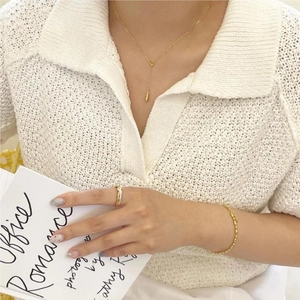 Close-up of elegant gold teardrop pendant necklace and ring on a model in white knitwear