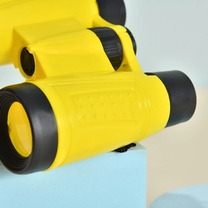 Close-up of yellow and black 6x30 children binoculars toy on a blue display block